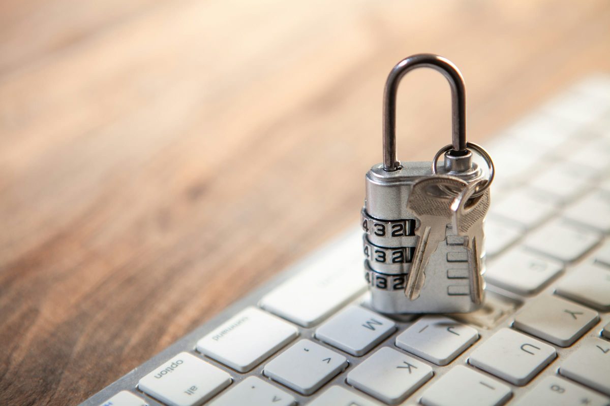 A silver combination lock with keys is placed on a white keyboard. The lock is partially open, and the keys are inserted into it.